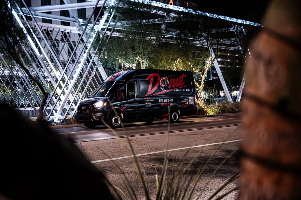 Black Donut Mobile Tire service van parked at night under a lit steel archway in Phoenix, Arizona